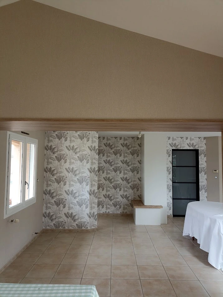 Rénovation intérieure réalisée par Ramboz Le Peintre incluant la peinture des murs et la pose de papier peint à motifs végétaux. La vue d'ensemble montre une harmonie entre les tons beiges des peintures et les revêtements muraux décoratifs.