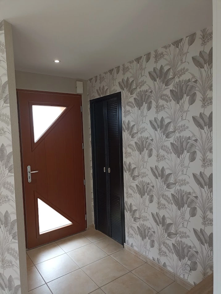 Pose de papier peint à motifs végétaux réalisée par Ramboz Le Peintre dans une entrée à Cholet. Le revêtement mural est ajusté aux menuiseries et au sol en carrelage pour une rénovation intérieure complète.